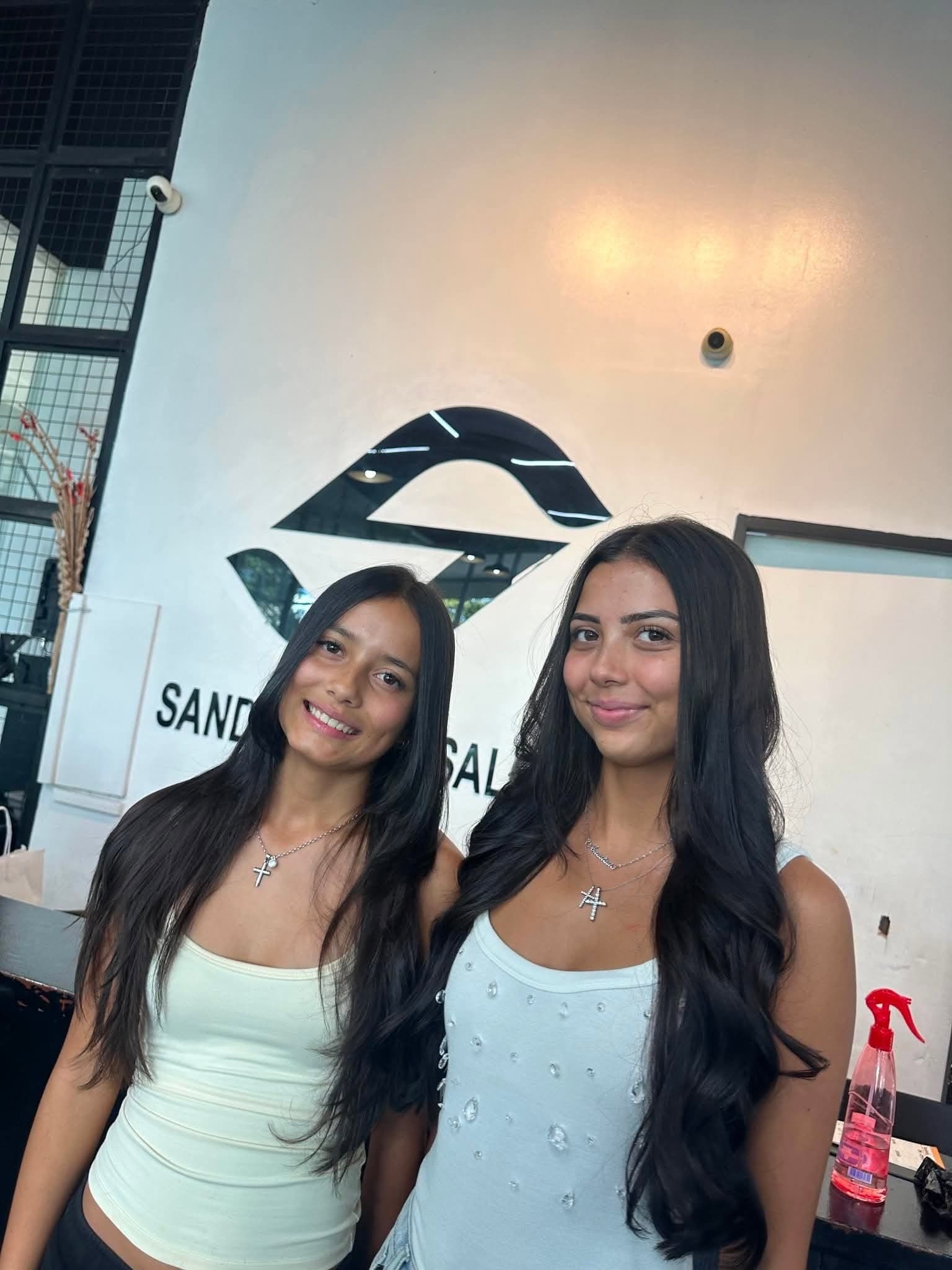 Two clients with long, voluminous styled hair in front of the SandreaLee sign